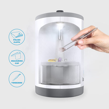 Jewelry cleaning device with a hand using tweezers and a measuring cup, on a white background.