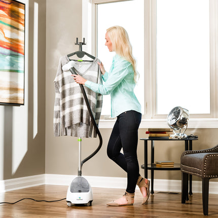 Woman using a garment steamer on a shirt in a room with a window and furniture.