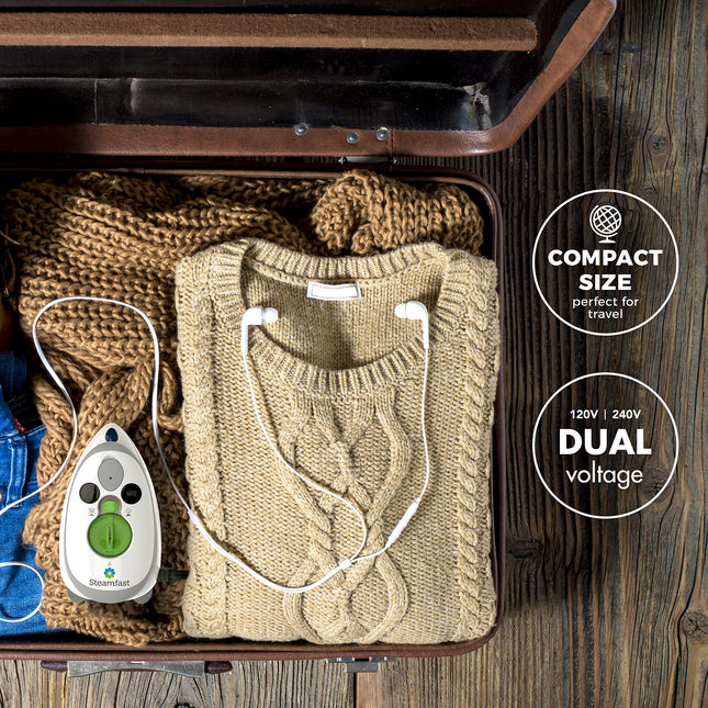 Folded sweater with a garment steamer in an open suitcase on a wooden floor.