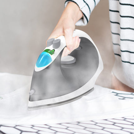 Person ironing fabric with a gray iron featuring a blue and green design on the handle.