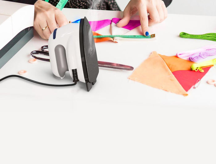 Person ironing fabric on a table with sewing machine and colorful materials