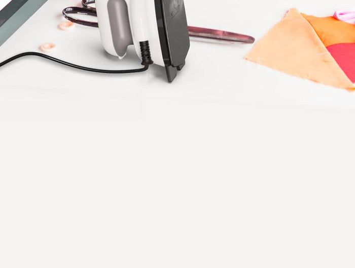 Person ironing fabric on a table with sewing machine and colorful materials